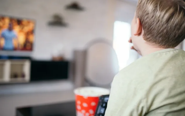 Gemütlicher Filmabend zu Hause: Ein Junge sitzt mit Popcorn vor dem Fernseher